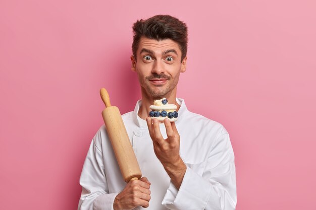 Pastry chef holds cream tasty cake, tells recipe of delicious confectionery, works in cafe as cook, dressed in white uniform