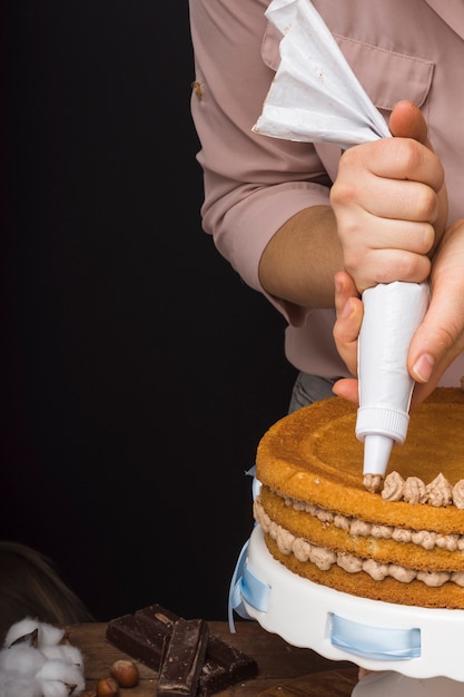 Pastry chef squeezing cream on cake