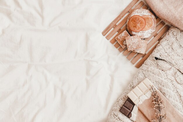 Pastry, chocolates with herb and plaid lying on white bedsheet