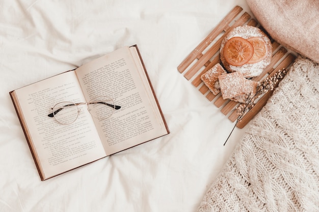 Pastry, eyeglasses lying on opened book on bed 