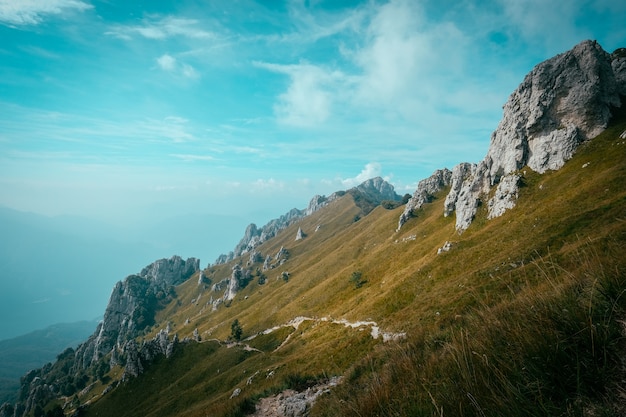 Free photo pathway on a hill in the middle of a grassy field with rocky cliffs with a blue sky