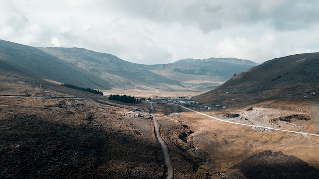 Pathway in the middle of mountains near a house under a cloudy sky