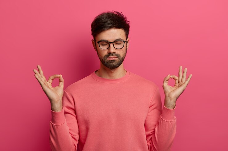 Free Photo patience, calmness and meditation concept. peaceful relieved bearded young man practices yoga exercise, keeps hands in zen gesture, closes eyes, poses over pink wall, controls his emotions