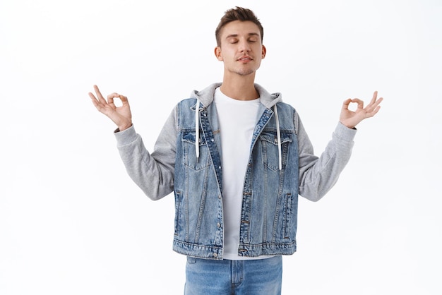 Free photo patience is key portrait of calm and relieved handsome blond young male student taking deep breath close eyes and meditating with hands sideways in zen sign reach nirvana practice yoga