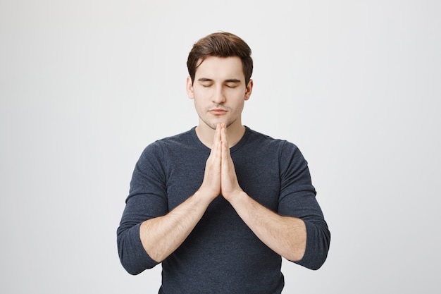 Free photo patient calm handsome guy praying, hold hands in plead gesture