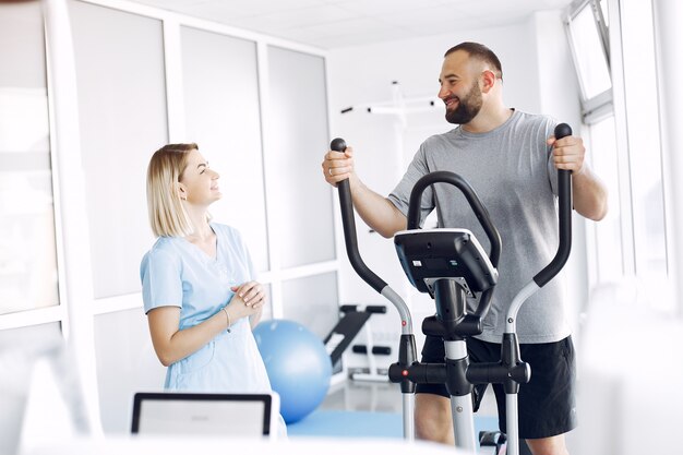 Patient doing exercise on spin bike in gym with therapist