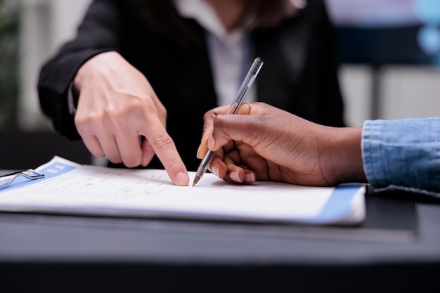 Patient filling in report papers at reception desk, signing registration forms before attending checkup visit appointment. Woman writing checkup files with receptionist, healthcare support. Close up.