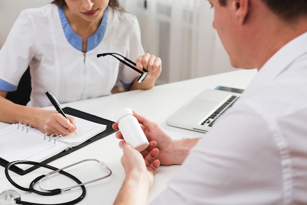 Patient hands holding pills while doctor is writing