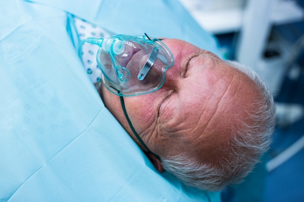 Patient lying on bed with oxygen mask in operation room