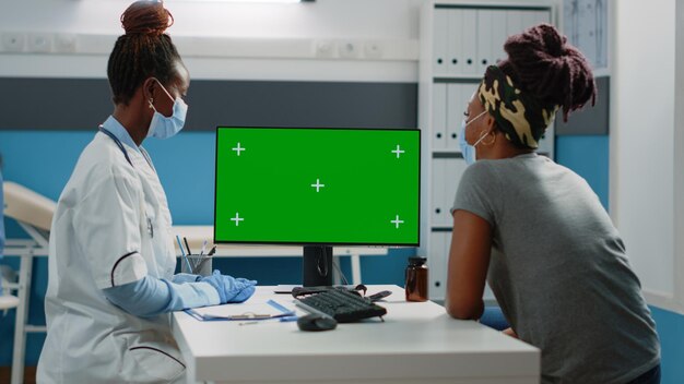 Patient and medic looking at horizontal green screen on monitor at desk. Doctor using computer with chroma key for mockup template and isolated background at checkup visit with woman.