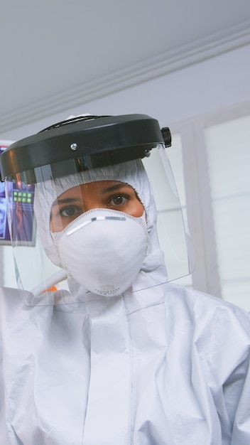 Free photo patient pov of dentist explaining teeth treatment wearing covid protective suit in new normal stomatological office. stomatolog in safety gear against coronavirus during heatlhcare check of patient.