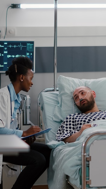 Patient talking with medical doctors while sitting in bed during disease recovery in hospital ward