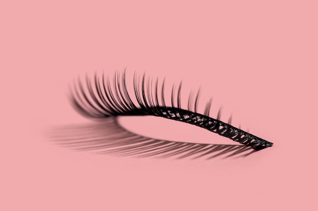 A pattern of separate false lashes on pink background with hard light makes shadow
