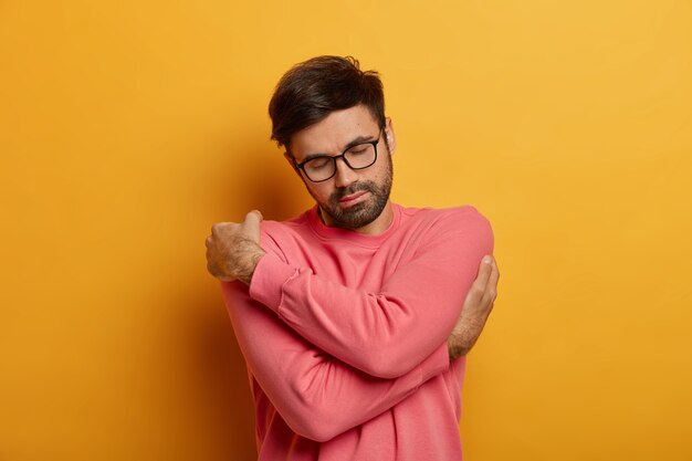 Peaceful bearded man crosses hands over body, feels comfort in his new sweater