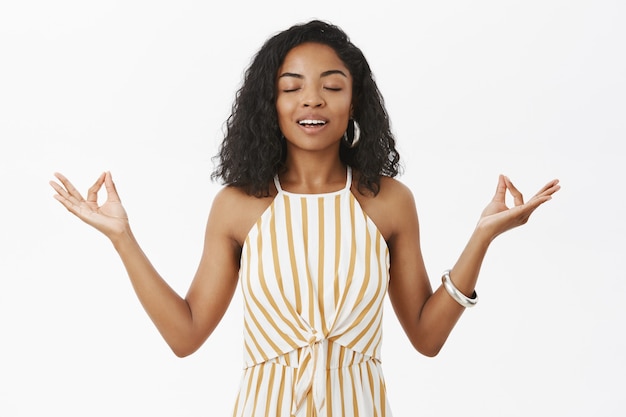 Free photo peaceful calm charming dark-skinned female model in yellow striped dungarees standing in lotus pose