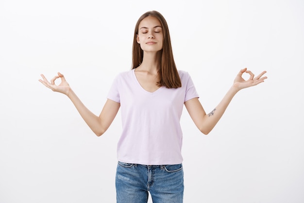 Peaceful charming chill european woman practicing yoga standing in lotus pose with fingers in zen gesture and closed eyes being determined while meditating