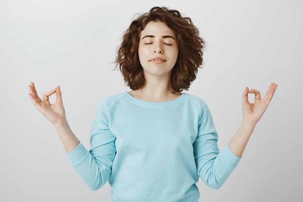 Free photo peaceful and relaxed smiling woman with closed eyes meditating to find zen