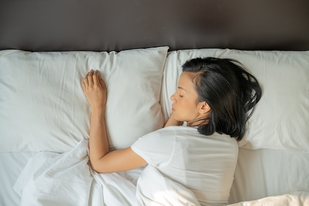 Peaceful serene young lady wear pajamas lying asleep on the bed. Top view