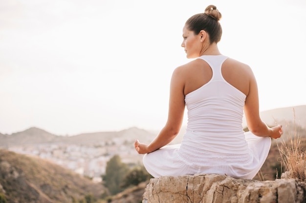 Free photo peaceful woman meditating on rock in front of city