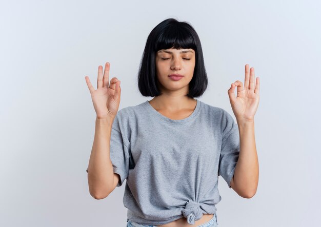 Peaceful young brunette caucasian woman stands with closed eyes pretending to meditate