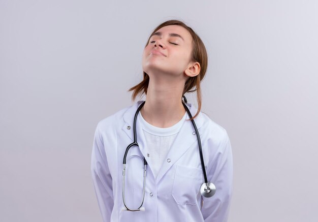 Peaceful young female doctor wearing medical robe and stethoscope raising head up with closed eyes  with copy space