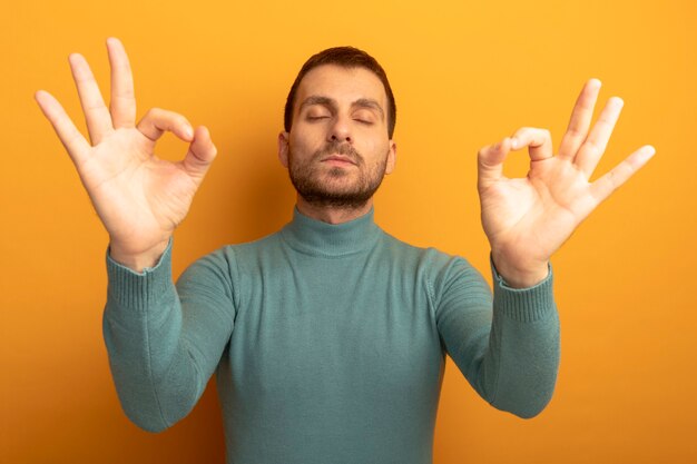 Peaceful young man doing ok signs with closed eyes isolated on orange wall