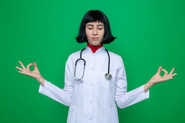 Peaceful young pretty caucasian woman in doctor uniform with stethoscope meditating with closed eyes 