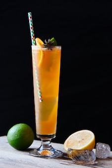 Персиковый черный чай со льдом состоит из ванильного сиропа, специй и лимонного сока в стеклянном крупном плане на деревянном столе на темном фоне