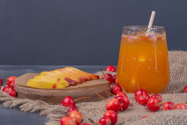 Ломтики персика, вишни и стакан фруктового сока на синем.