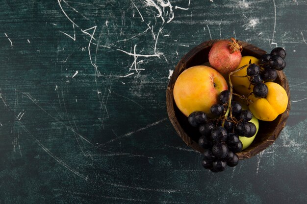 Peaches and grapes in a wooden bowl on black board