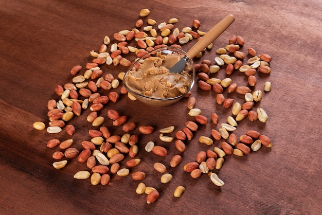 Peanut butter surrounded by peanuts on wooden horizontal