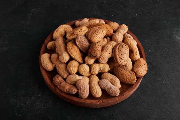 Peanuts and almond shells in a wooden plate on grey space. 