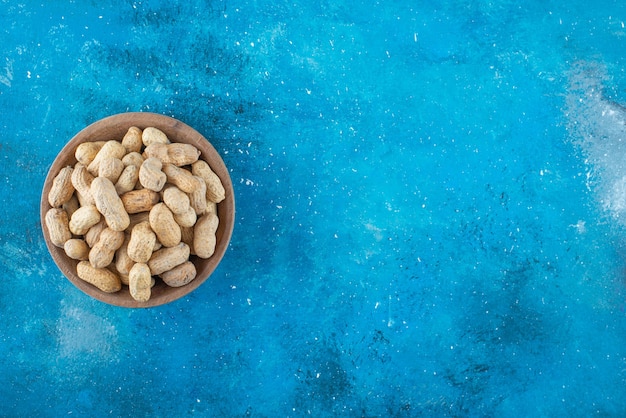 Peanuts in shell in a bowl on the blue surface