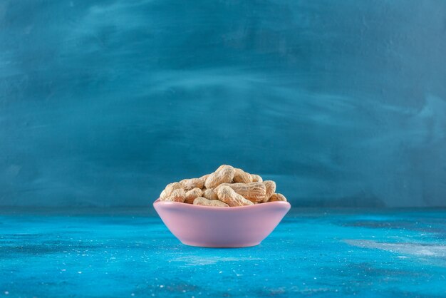 Peanuts in shell in a plate , on the blue table. 