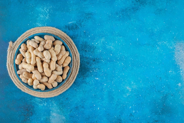 Peanuts in shell in a wooden plate on trivet on the blue surface