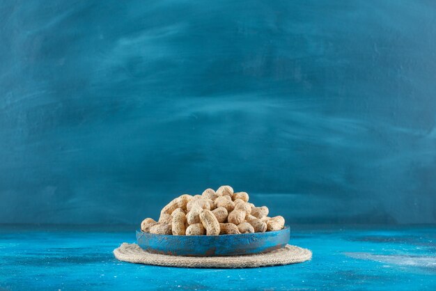 青いテーブルの上に、トリベットの木製プレートの殻のピーナッツ。