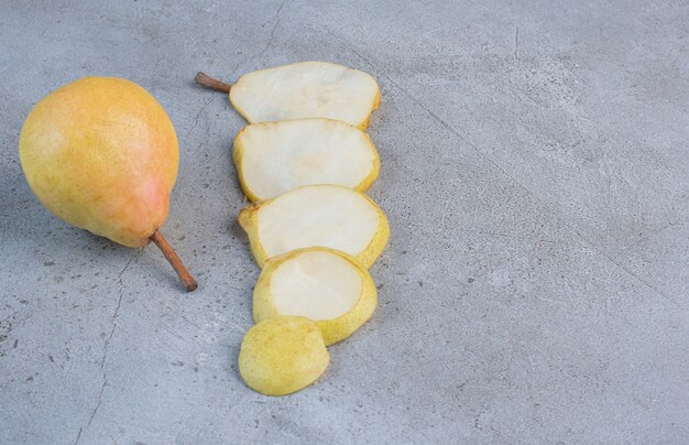 Pear slices lined up next to a whole pear on marble background. 