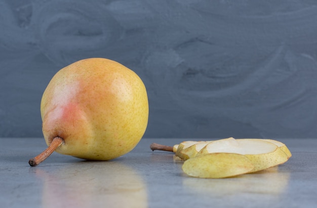 Pear slices lined up next to a whole pear on marble background. 