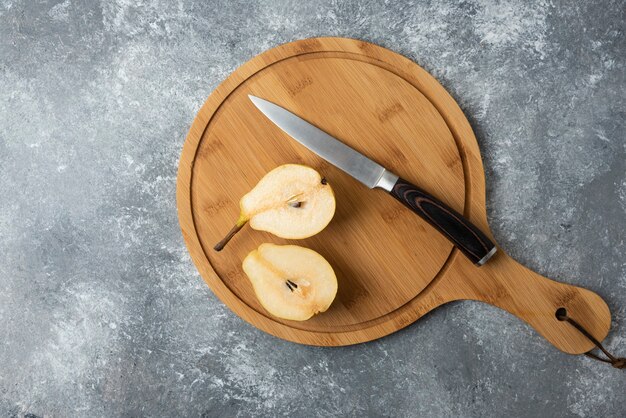 Ломтики груши на деревянной доске с ножом.