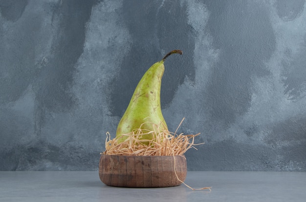 Pear in a tiny, straw-stuffed bowl on marble 