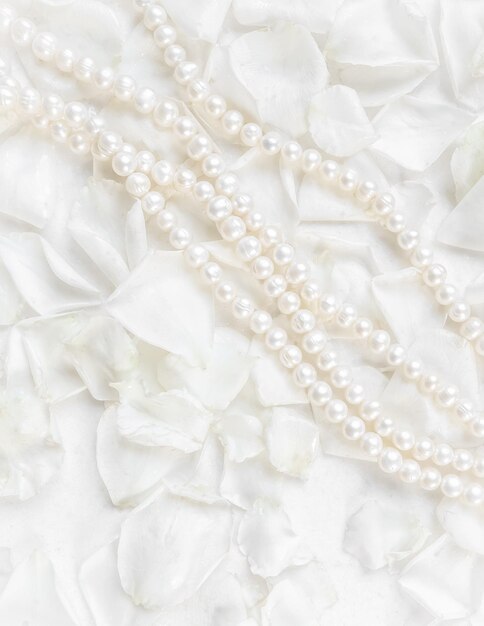 Pearl necklace on a background of white rose petals ideal for greeting cards for wedding birthday