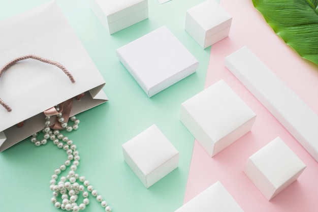 Pearls necklace falling from shopping bag with white boxes on pastel background