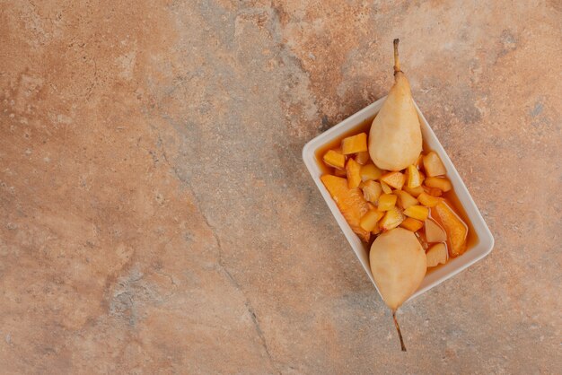 Pears and bowl of fruit jam on orange marble table.