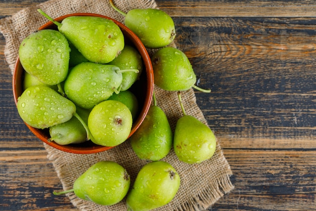 Pears in a bowl on wooden and piece of sack background. flat lay.