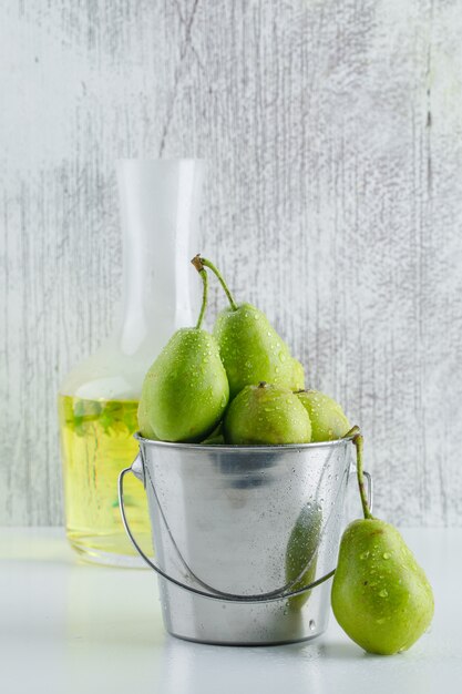 Pears in a mini bucket with herbal drink side view on white and grungy wall