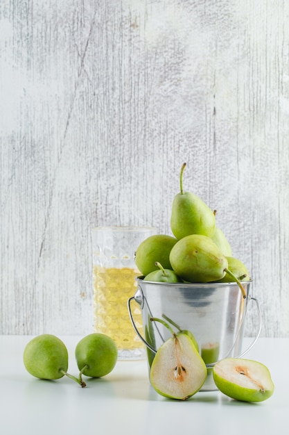 Pears with drink in a mini bucket on white and grungy wall, side view.