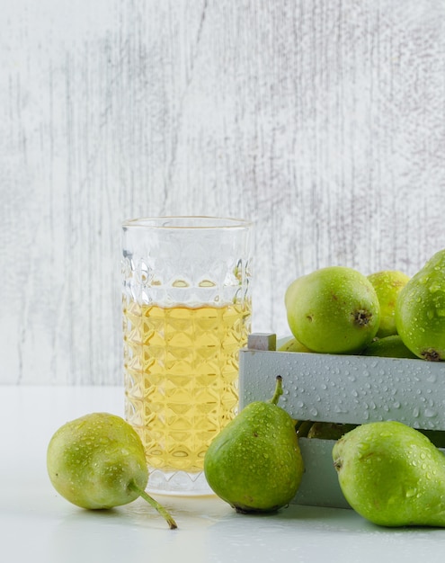 Pere con bevanda in una scatola di legno sulla parete bianca e sgangherata, vista laterale.