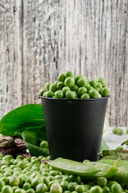 Peas in a mini bucket with bok choy, green pods, asparagus side view on a wooden grunge wall