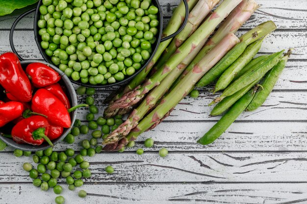Peas in a saucepan with peppers, asparagus, green pods top view on a wooden wall