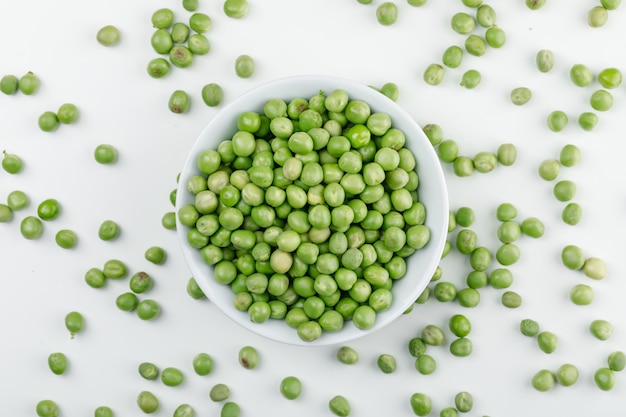 Peas in a white bowl top view on a white wall